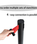Hand connecting red belt to the Premium 2 Pack Crowd Control Stanchions With 6.5 Foot Red Retractable Belts Steel Black Posts Non Slip Rubber