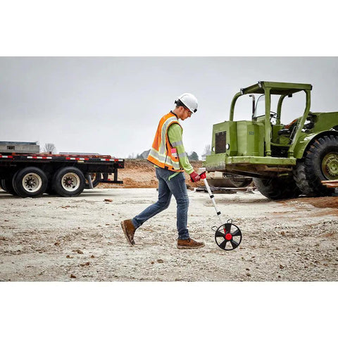 Person measuring ground distance with Built Different 12 Inch Digital Measuring Wheel Featuring Smooth Rubber Treader And Sturdy Spoked Frame Engineered For Precision Layouts And Heavy Duty Construction Projects Hooks Right Up With Milwaukee Gear.