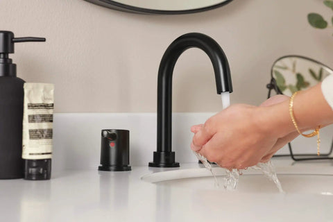 Person washing hands under Precept Widespread Matte Black Bathroom Faucet For 3-Hole 6-16 In. Install With ADA Push Pop-Up Drain