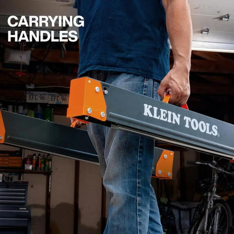 Carpenter carrying Tough As Nails Folding Sawhorses with orange handles in garage setting.