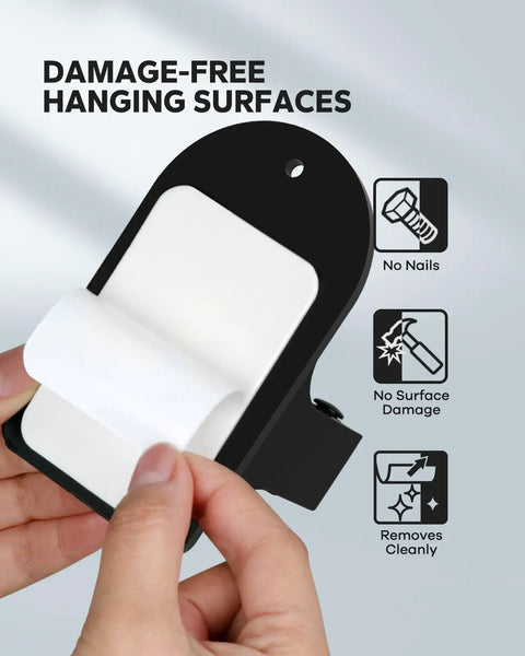 Hands holding adhesive strip of Beefy Heavy Duty Broom Holder Wall Mount Set Of 4 Black Metal Bracket showing damage-free features.