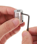 Person holding one of the Five Pack Aluminum Shaft Couplings 5mm To 6.35mm Flexible Motor Connectors with wrench, close-up view