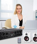 Bluetooth Wireless Home Amplifier System With 6 Channel Power 750 Watts, remote, and speakers on desk, woman using laptop