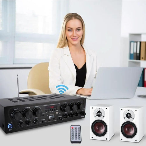 Bluetooth Wireless Home Amplifier System With 6 Channel Power 750 Watts, remote, and speakers on desk, woman using laptop