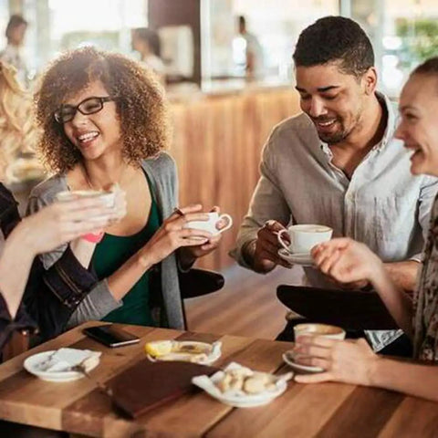 Four friends enjoying coffee together at a cafe, sharing conversation and laughter around a small table.