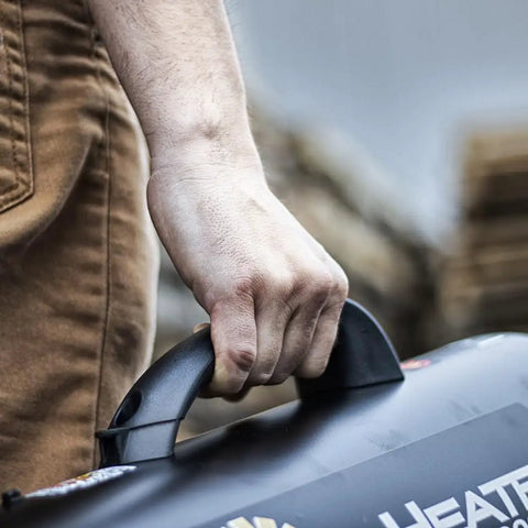 Close-up of a person holding the handle of a 60,000 BTU Portable Propane Forced Air Heater With Quiet QBT Technology, shown outdoors.
