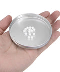 Ceramic bearing balls, 5 mm diameter, zirconia oxide, white; 28pcs in a metal lid held in hand (close-up).