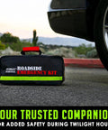 Everlit roadside emergency kit bag, black with neon green stripe and red handle, beside car tire.