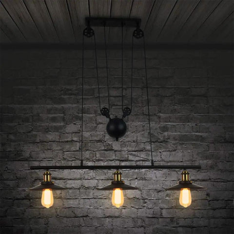 Drop Dead Modern Industrial Chandelier 3 Light Retractable Pulley Pendant with exposed bulbs over dark brick wall.