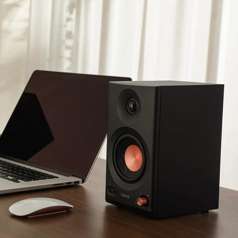 Black MR3 Powered Studio Monitors With Hi-Res Audio Certification And Bluetooth 5.4 next to a laptop and mouse on a desk.