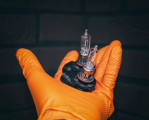 Orange nitrile glove holding two clear halogen headlight bulbs with orange bases