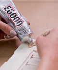 Hands applying All Purpose Craft Adhesive 3.7 Fluid Ounces Clear Bonds Glass Wood Plastic Ceramic Metal Leather Fabric Rubber on wood surface