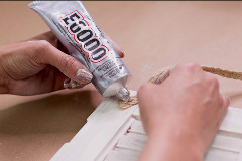 Hands applying All Purpose Craft Adhesive 3.7 Fluid Ounces Clear Bonds Glass Wood Plastic Ceramic Metal Leather Fabric Rubber on wood surface