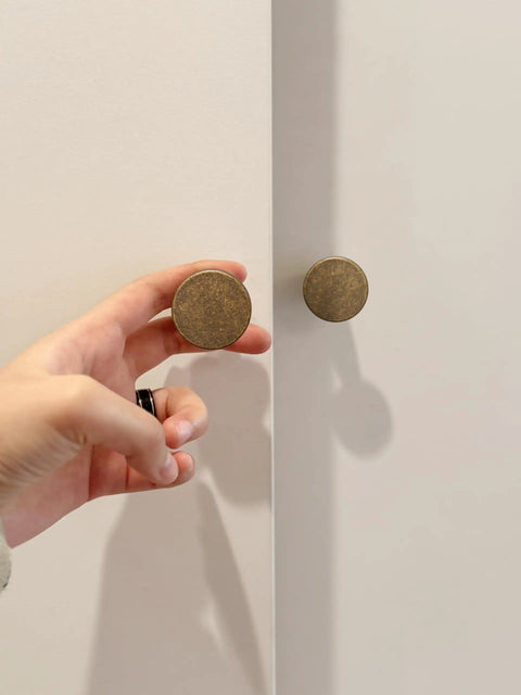 Hand holding knob from Antique Brass Cabinet Knob Set 6 Pack Solid Zinc Alloy Drawer Pulls for Kitchen Cabinets and Dressers