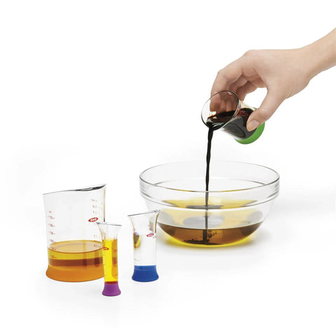 Hand pouring liquid from Go-To Nesting Measuring Beaker Set 7 Pieces Multicolored Kitchen Must-Have into a bowl
