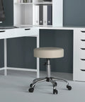 Ergonomic Adjustable Height Stool For Beauty Salons And Medical Spa With Plush Beige Cushioning Heavy Duty Chrome Swivel Base And Smooth Gas Lift in office setting.