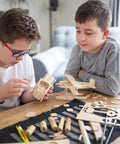 Unfinished basswood craft wood pieces for DIY projects; two boys assemble wooden model parts on a table