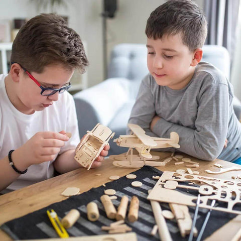 Unfinished basswood craft wood pieces for DIY projects; two boys assemble wooden model parts on a table