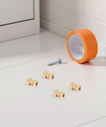 Brass Tee Pipe Fitting 3 Way Connector With Female Threads, Compact Block Design, on a white surface near orange tape and nail.
