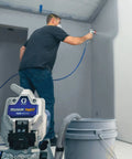 Pro Grade Airless Paint Sprayer With Fully Adjustable Pressure and a rugged stainless steel piston pump in use on a wall.