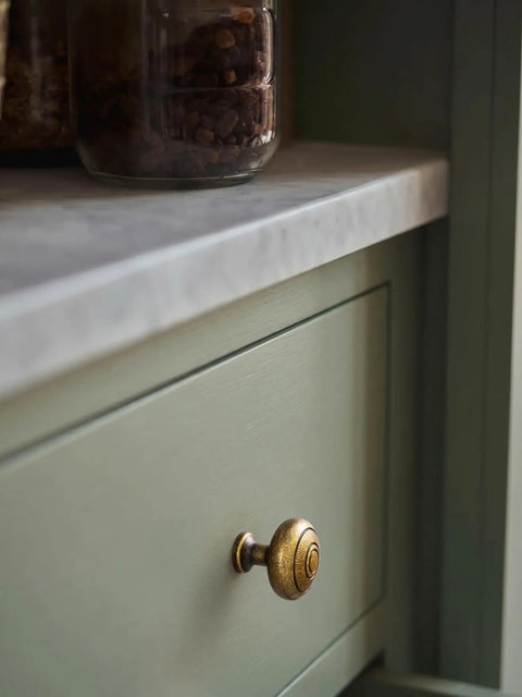 Real Deal Antique Brass Cabinet Knobs 1 1/4 Inch Round Sunburst Design on green cabinet drawer.