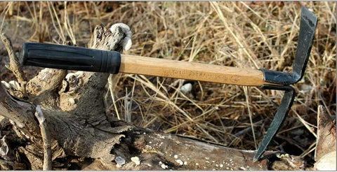Small Hand Held Garden Pick Mattock For Weeding And Cultivation with wooden handle, resting on a tree stump outdoors.
