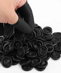 Hand picking black silicone finger cots from a pile, showcasing 100 Pack Black Silicone Finger Cots And Protective Toppers For Manicures And Massage Sessions Soft Disposable Fingertip Shields With A Snug Fit That Keeps Your Digits Locked In No Sweat Setup Top Shelf Quality Daily.