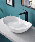 Oval Vessel Sink White Porcelain Ceramic Modern Above Counter Bathroom Basin With Pop Up Drain Included 23.6 Inch Long By 13.65 Inch Wide By 5.65 Inch Deep Slick Contemporary Design with water flowing from a black faucet on a marble countertop.