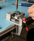 Heavy Duty Cast Iron Bench Vise With 360 Swivel Base gripping a circuit board for soldering on a workbench.