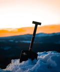 Adventure Mini Shovel 23 Inch Lightweight Aluminum Recovery Tool with wrinkle black coating in snow, sunset backdrop
