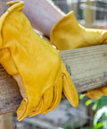 Person wearing heavy duty leather work gloves for men and women, yellow X large 3 pack, gripping a wooden beam securely.