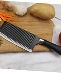 SOLUSTRE wavy chopper knife on cutting board with potatoes and garlic; stainless steel blade, black handle
