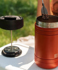 Insulated French Press Keeps Your Daily Joe Hella Hot For Hours With Tough Stainless Steel Build And Secure Twist Lid Crafted For Cabin Weeks And Backyard Chillin 32 Fl Oz Red Rock, showing coffee grounds being added.