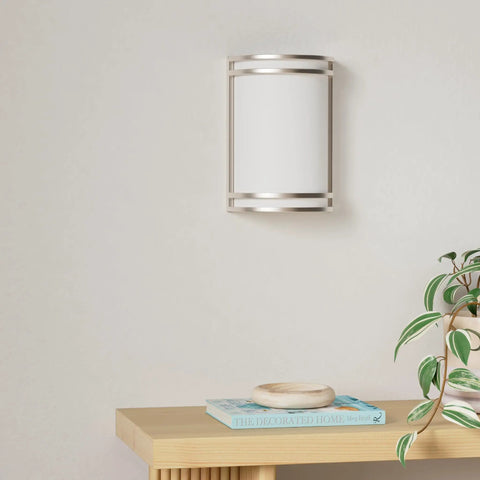 Kick Your Lighting Game Up Today With This Sleek Indoor LED Wall Sconce Sporting Brushed Nickel Finish And Adjustable 3000K 4000K 5000K Temps Plus Zero Hassle Mount And A Smooth Rust Proof Glow Built For Everyday Chill on wall with plant and book nearby.