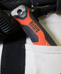 Klein Tools folding jab saw handle in orange and black, shown in a beige fabric pocket.