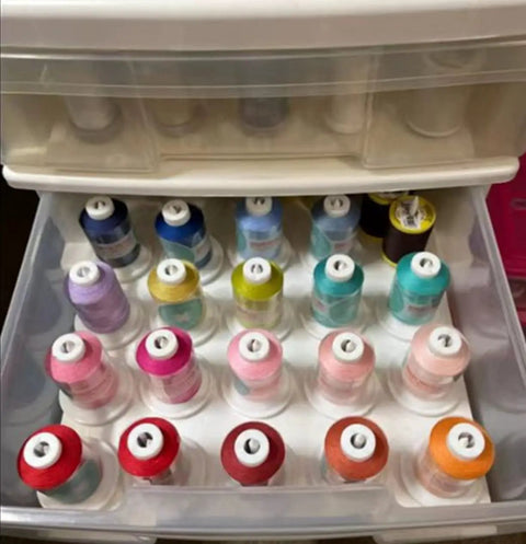 Drawer with colorful spools of thread neatly organized in rows, showcasing various shades for sewing and crafting projects.