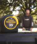 35 Foot Tape Measure With BladeArmor Coating On First 6 Inches, close-up showing front branding in front of blurred worker