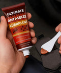Ultimate Anti-Seize Lubricant copper paste tube (1 oz) in hand, applying with white spatula to brake pad hardware