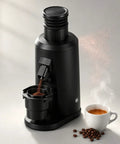 Badass 80mm Flat Burr Electric Coffee Bean Grinder With Straight Up Stepless Control And Rapid Brushless Motor For Seamless Daily Espresso Pulls And Relaxed Weekend Sips Black, grinding coffee with steaming cup beside.