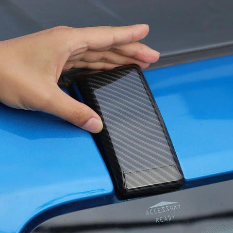Hand holding Premium Carbon Fiber Windshield Screw Covers For Ford Bronco 2021 To 2023 Left Right Pair near blue truck.