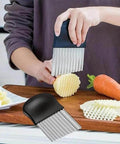 Crinkle cutter with a black handle and stainless steel blades slicing a potato on a cutting board.