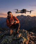 Man operating Air 3S Drone With RC 2 Fly More Bundle For Travel And Content Creation, Dual 4K Cameras, over mountain landscape at sunset.