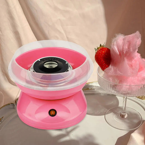 Pink cotton candy maker with clear plastic marshmallow dispenser cover next to a glass with cotton candy and strawberry.