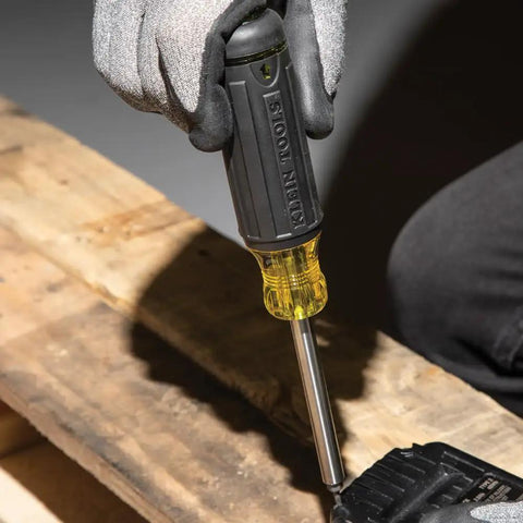 Gloved hand using Grab And Go Multi Bit Tamperproof Screwdriver Kit With Twenty Six Onboard Bits And Quarter Inch Nut Driver on wood