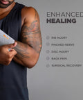 Person wearing gray wrist sleeve for pain relief and recovery, unisex size S/M, against enhanced healing backdrop.