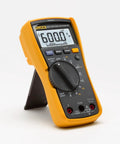 Digital Multimeter With Non Contact Voltage Detection VoltAlert Technology AutoVolt Automatic AC And DC Voltage Selection Low Impedance Mode To Prevent Ghost Readings Measures Resistance Continuity Frequency Capacitance Min Max And Average LED Backlight, yellow case, front view, on stand.