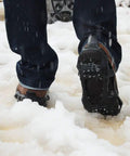 Person walking on snow wearing Slip On Ice Cleats Traction Crampons For Snow And Ice, Non Slip Rubber Overshoes with Stretch Fit, X Large Size.