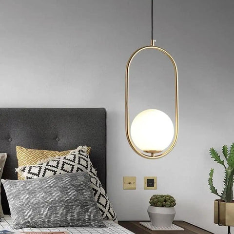 BEQAOR Modern Globe Pendant Light, 1-Light Oval Hoop Hanging Ceiling Fixture with Frosted White Glass Shade and Gold Finish Frame for Bedroom Bedside above a bed with pillows.
