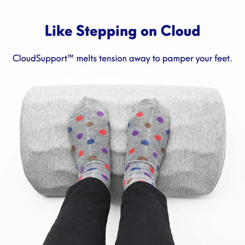 Feet in polka dot socks resting on Ergonomic Under Desk Foot Rest With Massage Ridge Design And Memory Foam Pillow For Work At Home Or Gaming Setup A Comfy Foot Stool That Eases Back And Hip Pain And Reduces Foot Swelling While You Sit All Day.