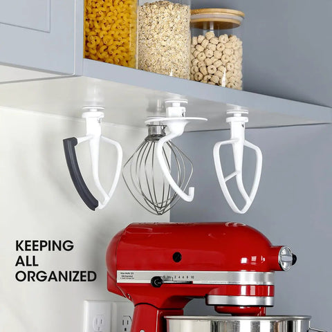 Installed Four Pack Stand Mixer Attachment Organizer For KitchenAid Accessories With Flex Edge Beater Flat Beater Dough Hooks And Wire Whip Universal Holder Rack For Grab And Go Access And Kitchen Counter Space under a kitchen cabinet, holding mixer attachments.